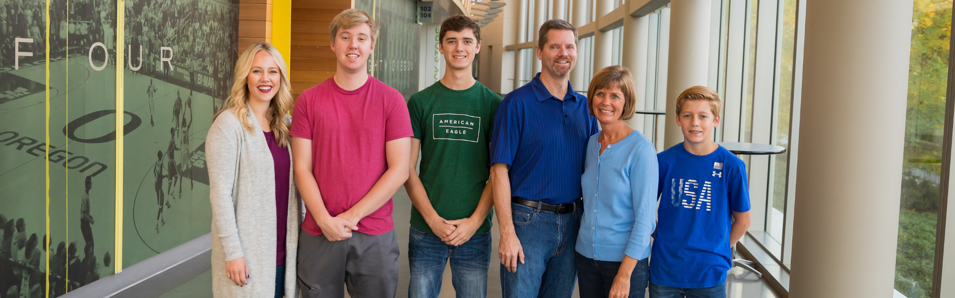 Smiling family standing together inside a building hallway, Dr. W. Gray Grieve Orthodontics, Eugene, OR