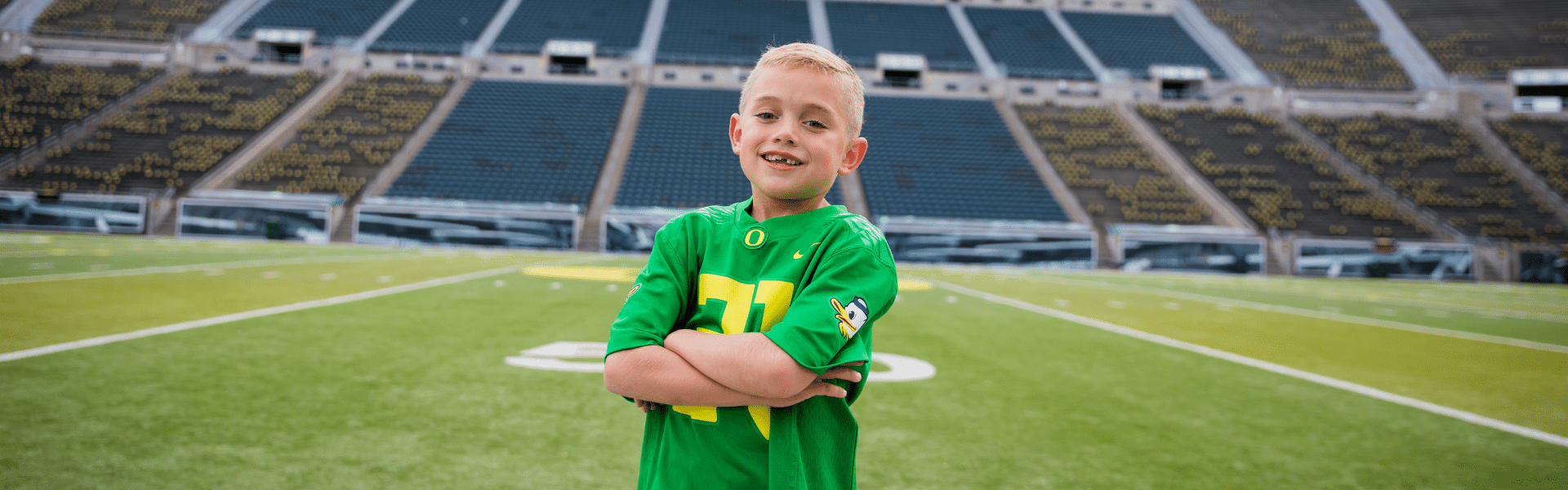 Smiling child patient wearing an Oregon Ducks football jersey while standing on a football field, Dr. W. Gray Grieve Orthodontics, Eugene, OR