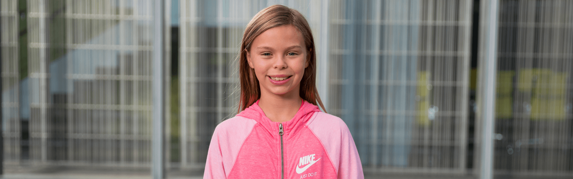 Smiling child patient wearing a pink Nike jacket while standing outdoors, Dr. W. Gray Grieve Orthodontics, Eugene, OR