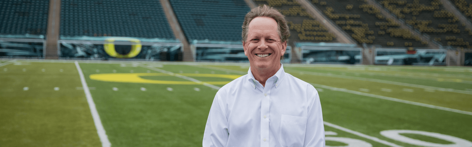 Portrait of Dr. Gray Grieve smiling on a football field with stadium seats in the background, Dr. W. Gray Grieve Orthodontics, Eugene, OR
